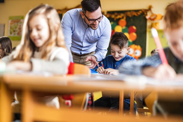 istock Young happy professor assisting his elementary students on a class at school. 1213693764