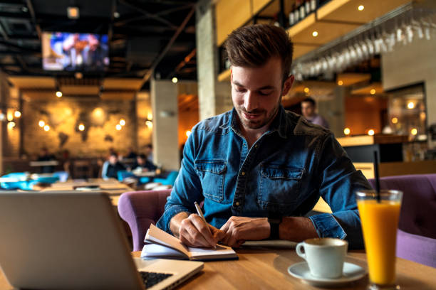 istock Freelancer working at cafe sitting at the table using laptop and writes in a notebook. 1213696928