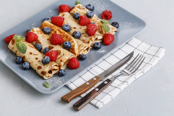 istock Twisted thin pancakes with raspberries and blueberries decorated with mint. Food on a gray square plate. Russian kitchen. 1213702687
