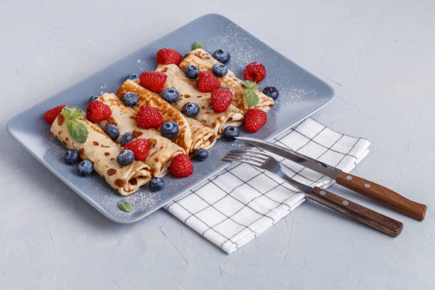 istock Twisted thin pancakes with raspberries and blueberries decorated with mint. Food on a gray square plate. Russian kitchen. 1213702702