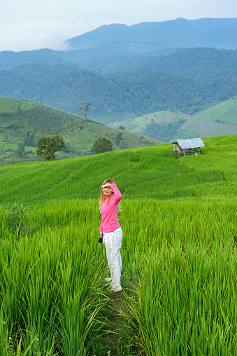 Thai woman standing in the green rice field with mountain and clouds background in Chiang Mai, Thailand.
