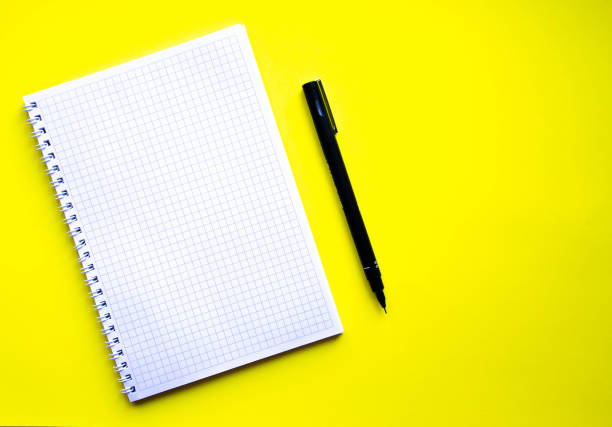 istock Squared notebook on a yellow background. Green and black pen and notebook. Notebook, planner. Place for text. Notebook with a spiral.  Copy Space 1213707382