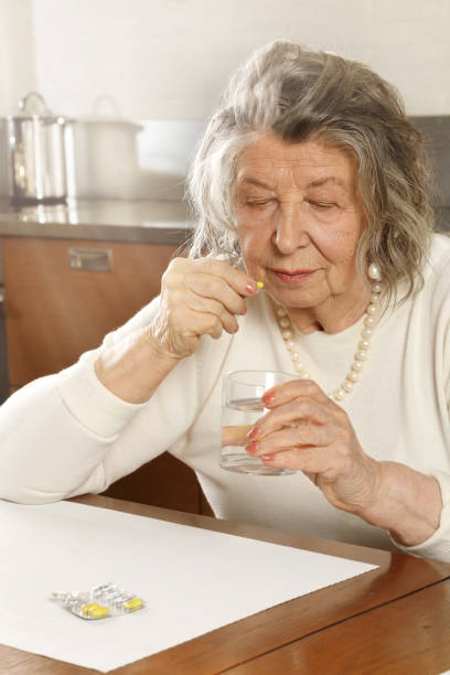 istock White-haired old woman sitting at a table taking pills 1213707806