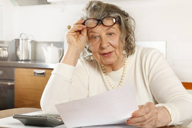 istock White-haired old lady looking through receipts with a calculator 1213707812