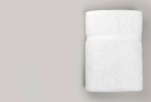 Photo of Top view of folded clean white bathroom towel on gray background with copy space