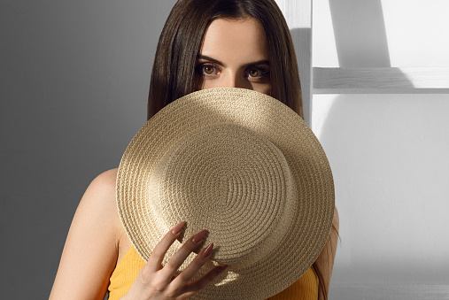 Attractive girl covering her face with straw hat in dramatic sun light on her eyes with ladder in background
