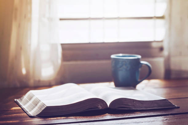 The holy bible and a cup of coffee on table close up of open bible with a cup of coffee for morning devotion on wooden table with window light religious text stock pictures, royalty-free photos & images
