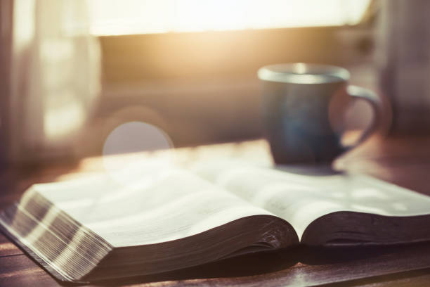 The holy bible and a cup of coffee on table close up of open bible with a cup of coffee for morning devotion on wooden table with window light preacher photos stock pictures, royalty-free photos & images