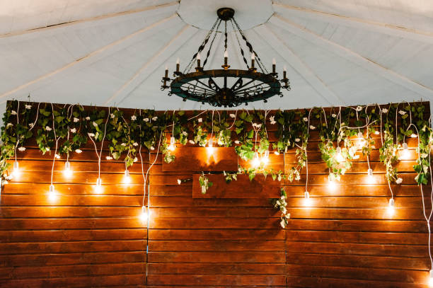 Festive arch over table decorated with composition flowers and greenery in the banquet hall. Banquet area on wedding party. Wooden decor. Wall with lamps and lights. Festive arch over table decorated with composition flowers and greenery in the banquet hall. Banquet area on wedding party. Wooden decor. Wall with lamps and lights. wedding hall stock pictures, royalty-free photos & images