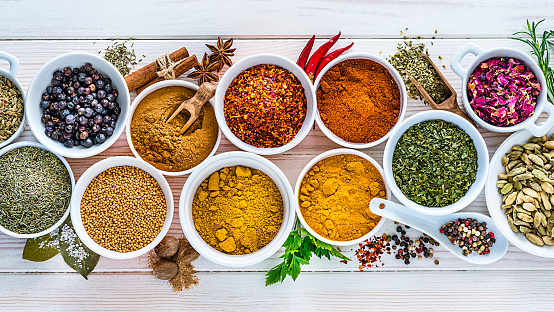 Indian food: top view of multi colored spices placed side by side on white table. The composition includes cardamom, rosemary, parsley, star anise, curry powder, bay leaves, nutmeg, salt, pepper, chili pepper, cinnamon sticks, turmeric, paprika, mustard seeds and oregano . High resolution 42Mp studio digital capture taken with Sony A7rII and Sony FE 90mm f2.8 macro G OSS lens