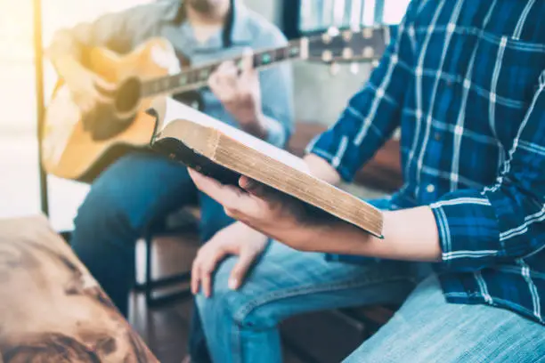 close up of a man holding hymn books and sing a song while his friend playing guitar, praise and worship concept