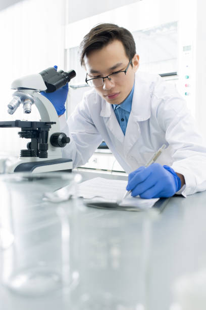 istock Chinese male lab worker in gloves and whitecoat making notes in notepad 1213725825