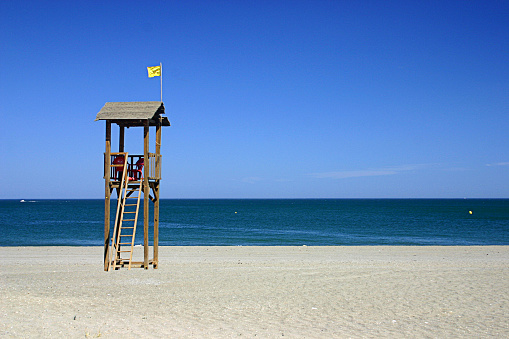 Beach equipped with orange and yellow deckchairs and umbrellas. The sand is golden. In the background panoramic view of Peschici.