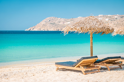 Mykonos beach during summer with umbrella and luxury beach chairs beds, blue ocean with mountain at Elia beach Mikonos Greece beach