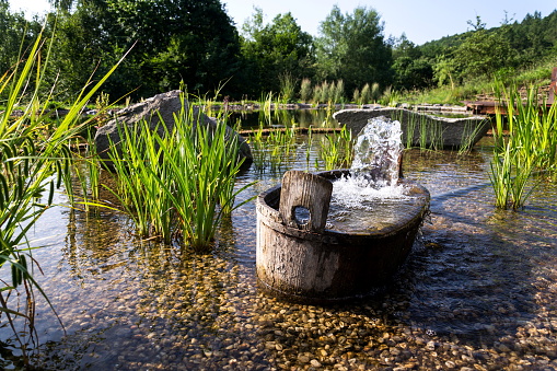 Wooden bucket with oxygenating flowing water at natural swimming pond or pool purifying water without chemicals through biological filters and plants