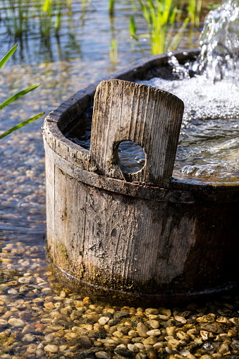 Wooden bucket with oxygenating flowing water at natural swimming pond or pool purifying water without chemicals through biological filters and plants