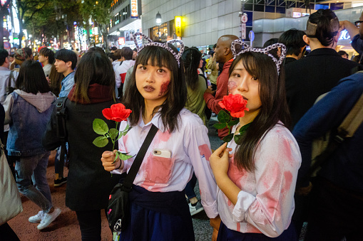 Tokyo, Japan - October 31, 2018: Two local women dressed in matching halloween costumes with cat ears and carrying roses hold hands as they move along the busy street in Tokyo’s famous Shibuya district all-night Halloween celebration.