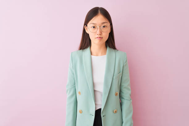 молодая китайская бизнесвумен в куртке и очках на изолированном розовом фоне с серьезным выражением лица. простой и естественный взгляд на - life jacket despair business life стоковые фото и изображения