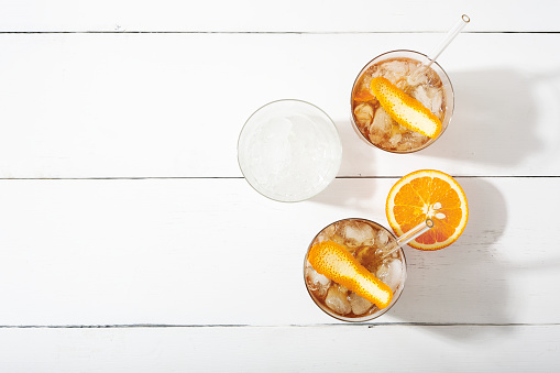 Cold brew coffee mocktail with orange peel and straw. Glass with citrus esprecco tonic and ice on white background top view flat lay. Refreshing summer drink concept. Horizontal orientation,copy space