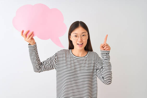 istock Young chinese woman holding cloud speech bubble over isolated white background surprised with an idea or question pointing finger with happy face, number one 1213735447
