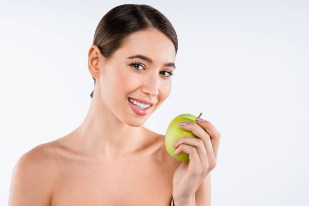 istock Happy attractive woman holding fresh apple and looking at it while standing against white background. Skin care concept 1213737601