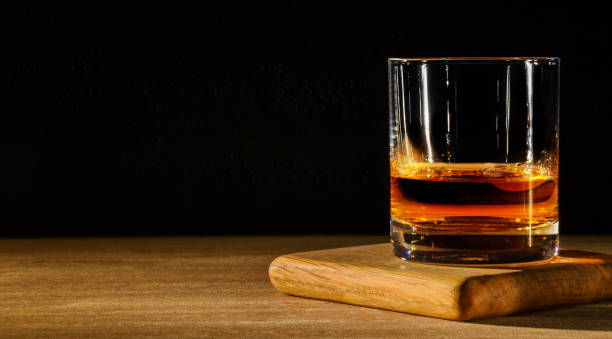 Glass with whiskey on wooden table and black background. Copy space. Glass with whisky on wooden table and black background. amber black photography stock pictures, royalty-free photos & images