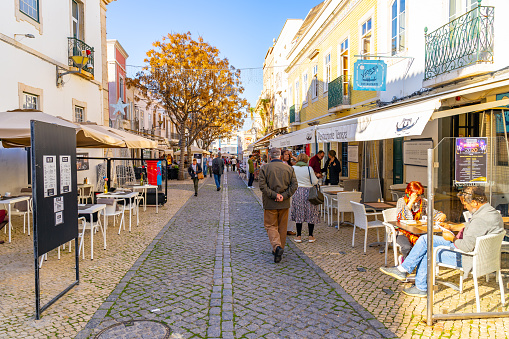 This pic shows old town of lagos city in portugal. Steet cafe, cobbledstoned street and some tourits can be seen in the pic. The pic is taken in day time in january 2020.