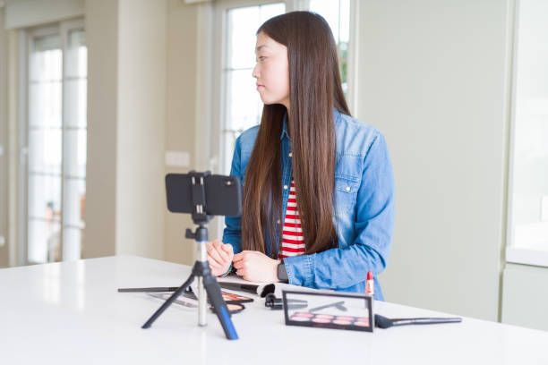 istock Beautiful Asian influencer woman recording make up tutorial using smartphone camera looking to side, relax profile pose with natural face with confident smile. 1213742663