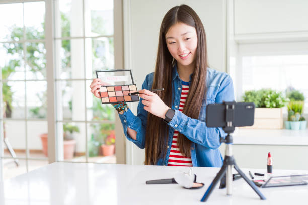 istock Beautiful Asian influencer woman recording make up tutorial using smartphone camera with a happy face standing and smiling with a confident smile showing teeth 1213742733