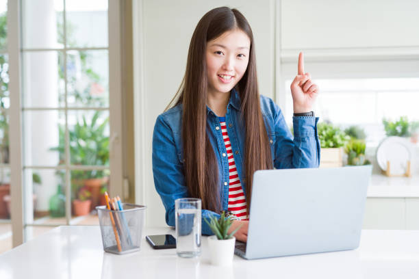 istock Beautiful Asian woman working using computer laptop surprised with an idea or question pointing finger with happy face, number one 1213743123