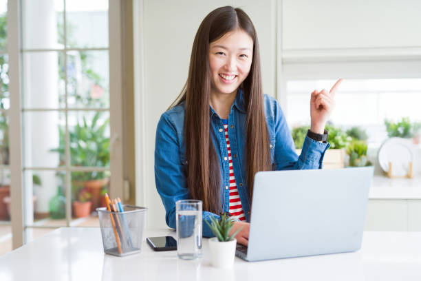 istock Beautiful Asian woman working using computer laptop very happy pointing with hand and finger to the side 1213743244