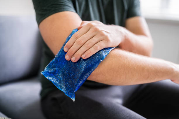 man using ice gel pack on arm - ice pack fotos imagens e fotografias de stock