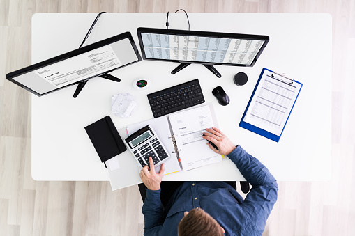 Young Businessman Calculating Bill With Computer And Laptop On Desk