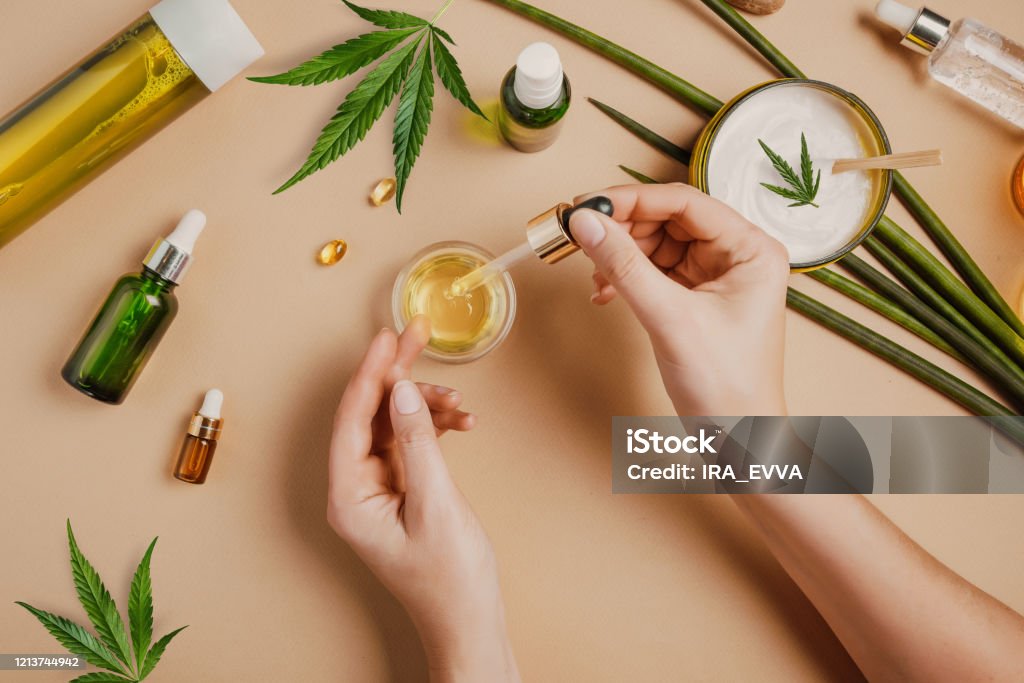 Pipette with CBD cosmetic oil in female hands on a table background with cosmetics, cream with cannabis and hemp leaves, marijuana Pipette with CBD cosmetic oil in female hands on a table background with cosmetics, cream with cannabis and hemp leaves, marijuana. Flat lay, top view. Cannabidiol Stock Photo
