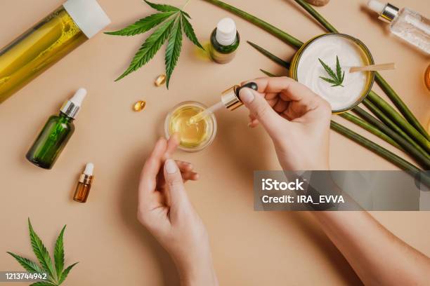 Pipette With Cbd Cosmetic Oil In Female Hands On A Table Background With Cosmetics Cream With Cannabis And Hemp Leaves Marijuana Stock Photo - Download Image Now