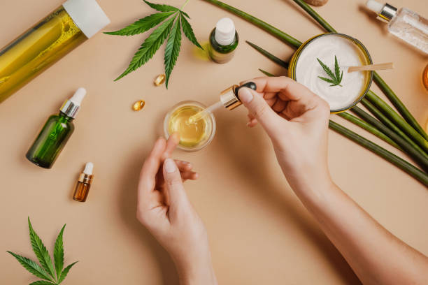 pipette with cbd cosmetic oil in female hands on a table background with cosmetics, cream with cannabis and hemp leaves, marijuana - moisturizer cosmetics merchandise human hand imagens e fotografias de stock