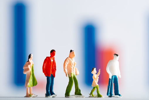 Selective focus of row of people figures on white surface with graphs at background, concept of equality