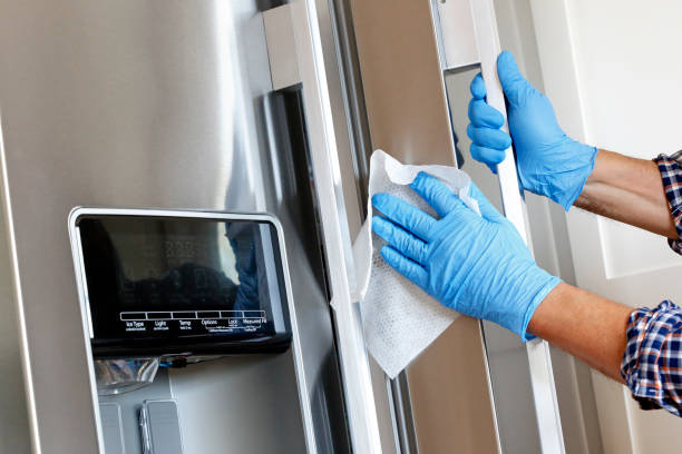 Man Cleaning Refrigerator With Disinfectant Wipe A close up of a Hispanic man wearing disposable gloves as he cleans a stainless steel refrigerator door handle with a disinfectant wipe. fridge clean stock pictures, royalty-free photos & images