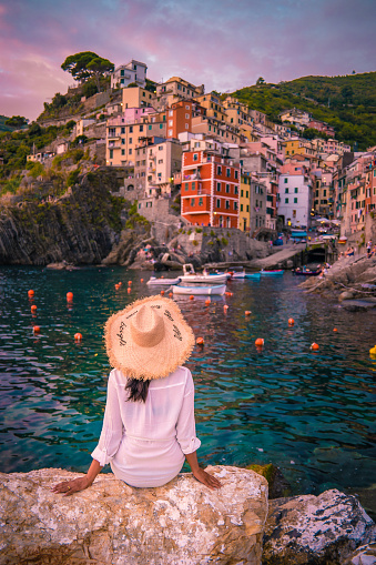 Riomaggiore Cinque Terre Italy , colorful village harbor front by the ocean, young woman watching sunset Italy