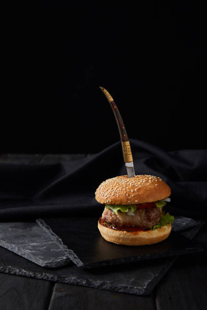 istock knife pierced in hamburger on dark cutting boards isolated on black 1213750687