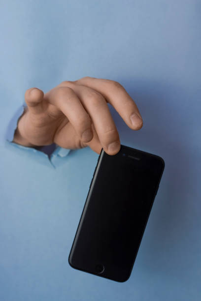 istock Men's hands squeamishly holds smartphone through a hole in torn blue paper 1213750904