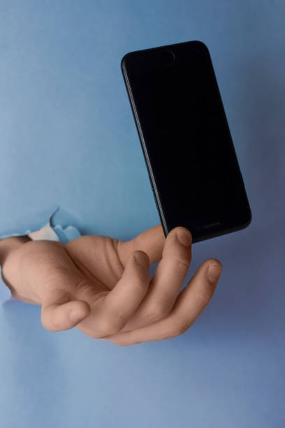 istock Men's hands squeamishly holds smartphone through a hole in torn blue paper 1213751006
