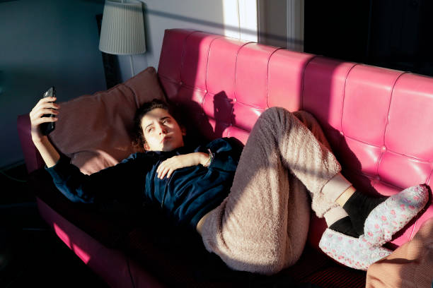 adolescente deitada em um sofá vermelho, olhando para seu celular - text messaging mobile phone teenagers only people - fotografias e filmes do acervo