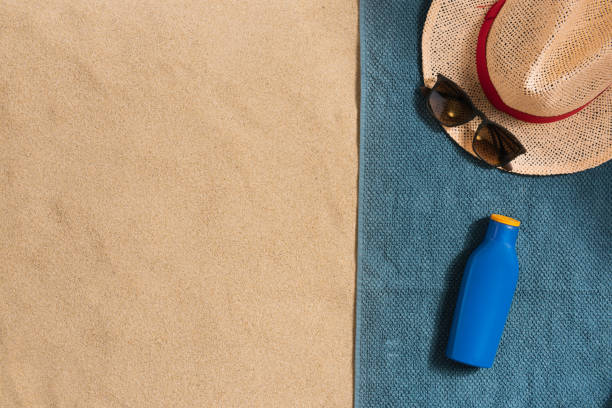 Summer vacation composition. Hat, sun cream and sunglasses on sand background. Harsh light with shadows. Summer background. Border composition made of towel stock photo