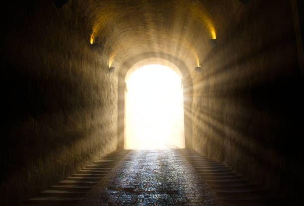 una luce luminosa giallo brillante che sfonda alla fine di un tunnel buio - luce alla fine del tunnel foto e immagini stock