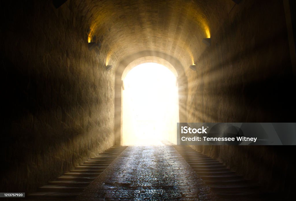 A bright yellow glowing light breaking through at the end of a dark tunnel Light - Natural Phenomenon Stock Photo