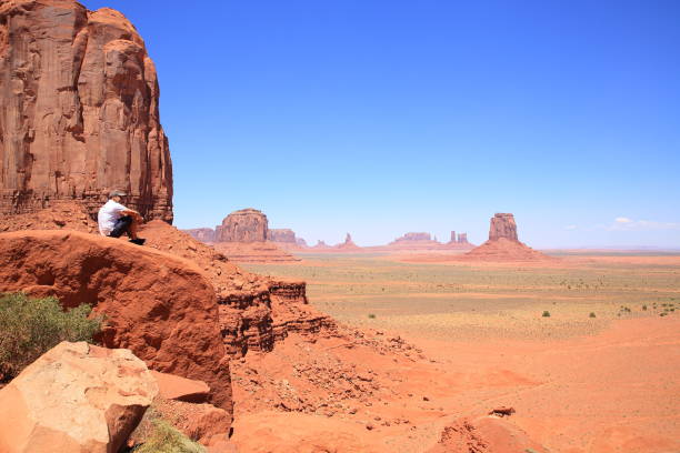Monument Valley, Arizona State-USA, August 14, 2019 : A male tourist sit on a rock and enjoy the Monument Valley on a summer day.