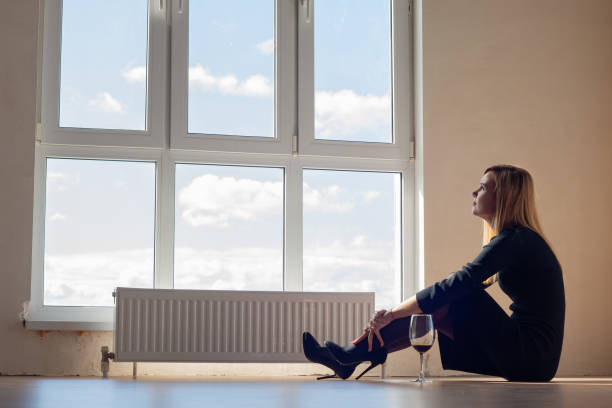 ワインのグラスと空のアパートの窓のそばに座っている悲しい女の子 - eastern european caucasian one person alcoholism ストックフォトと画像