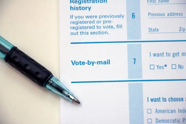 Closeup of 'Vote-by-mail' section on a voter registration form, with ballpoint pen laying on the form.