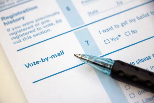 Closeup of 'Vote-by-mail' section on a voter registration form, with ballpoint pen laying on the form.